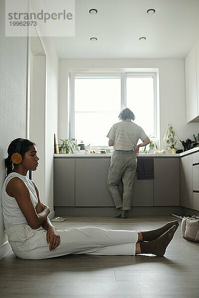 Teenage girl listening to music sitting on floor in kitchen