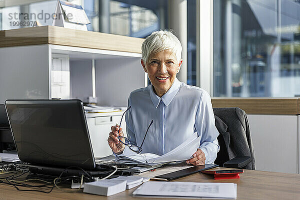 Lächelnde ältere Geschäftsfrau  die am Arbeitsplatz sitzt