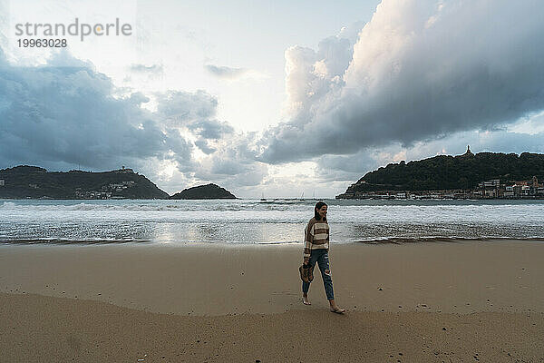 Junge Frau spaziert am Ufer der Playa de la Concha unter bewölktem Himmel