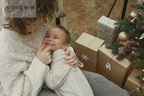 Liebevolle Mutter umarmt Sohn in der Nähe von Weihnachtsgeschenken zu Hause