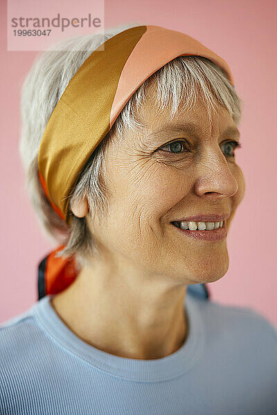 Lächelnde reife Frau mit Kopftuch vor rosa Hintergrund