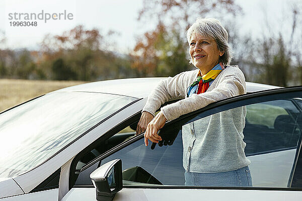 Lächelnde reife Frau  die neben der Autotür steht