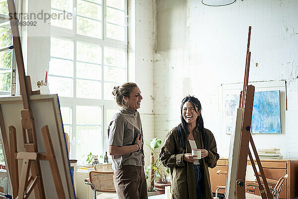 Fröhliche Frauen diskutieren über das Malen auf der Staffelei im Kunstatelier