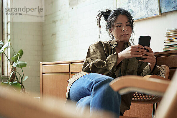 Künstler sitzt auf Stuhl und benutzt Smartphone in Werkstatt