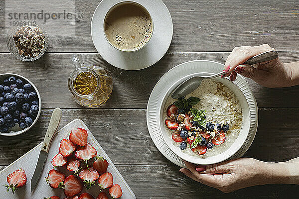 Hands of woman eating bowl of porridge with blueberries and strawberries