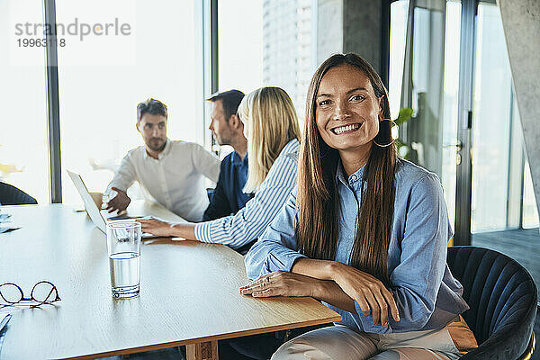 Glückliche Geschäftsfrau sitzt mit Kollegen im Hintergrund