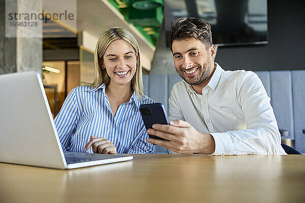 Zufriedene Geschäftskollegen nutzen Smartphone am Schreibtisch