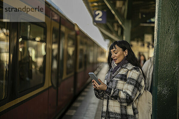 Frau benutzt Smartphone und steht am Zug  der am Bahnsteig ankommt