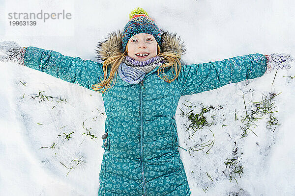 Playful girl wearing parka jacket and making snow angel