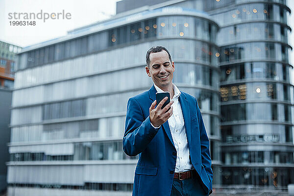 Glücklicher Geschäftsmann nutzt Smartphone in der Nähe von Gebäuden