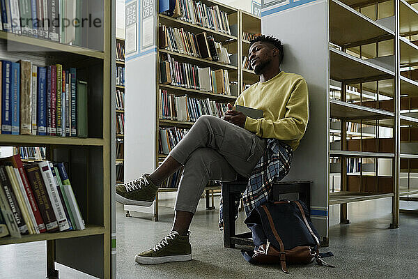 Student resting near bookshelves in library