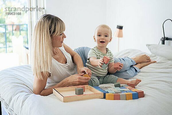 Mutter und Sohn spielen zu Hause mit Bauklötzen im Bett