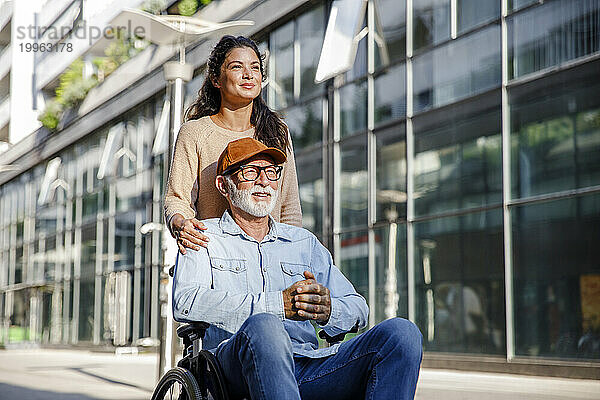 Lächelnder Sozialarbeiter hinter älterem Mann im Rollstuhl