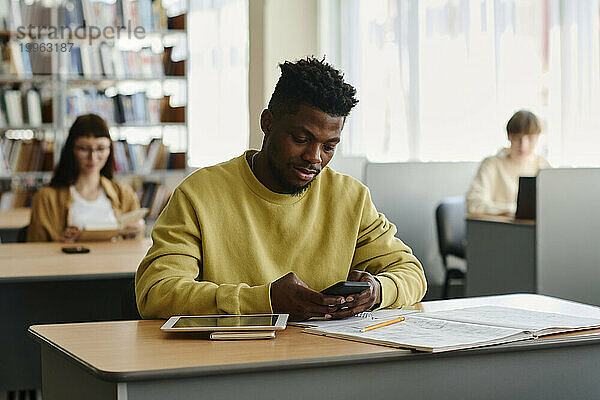 Junger Student nutzt Smartphone in der Bibliothek der Universität