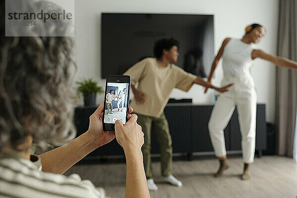 Mutter benutzt Smartphone und filmt Videos  in denen ihre Kinder zu Hause tanzen