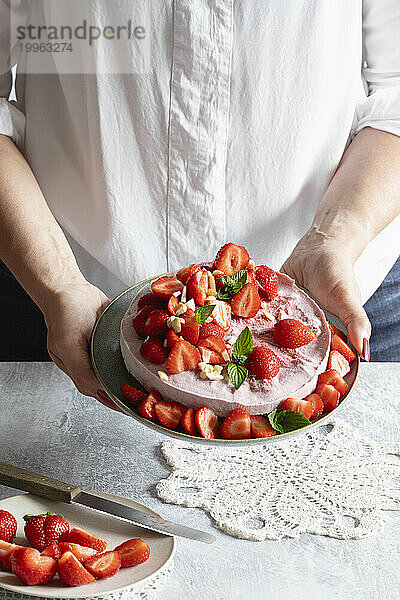 Hände einer Frau halten einen Teller mit verzehrfertiger veganer Erdbeertarte