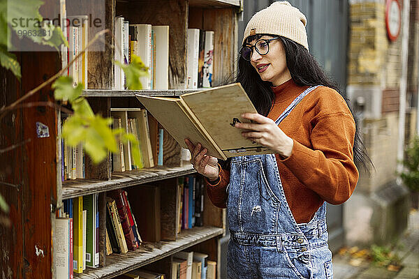 Lächelnde Frau mit Strickmütze liest Buch in Buchhandlung