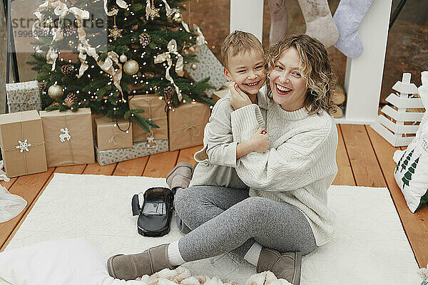 Glückliche Mutter und Sohn auf dem Teppich neben dem Weihnachtsbaum zu Hause