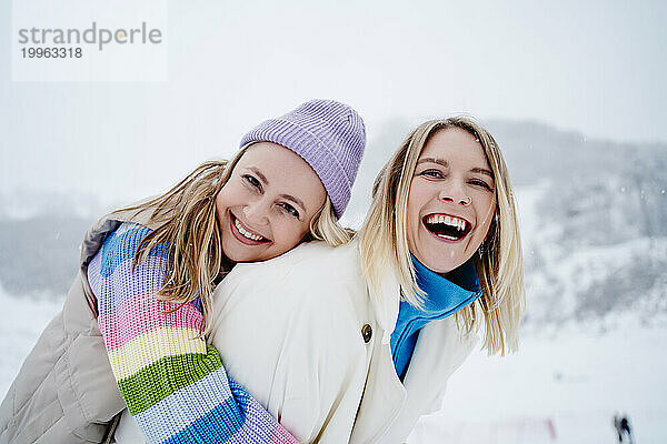 Glückliche Frau umarmt Freundin auf schneebedecktem Berg