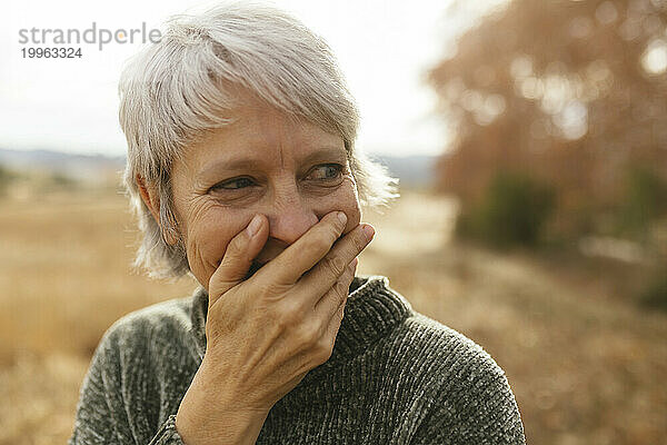 Happy woman with gray hair covering mouth and laughing