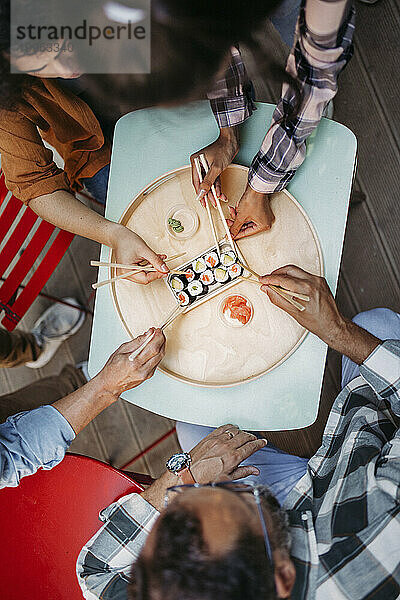 Hände multikultureller Freunde  die Sushi mit Stäbchen essen