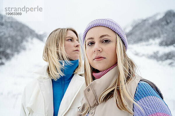 Blonde Frau trägt Strickmütze und steht im Winter mit einer Freundin