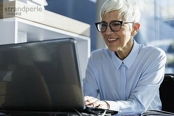 Glückliche Geschäftsfrau mit Brille und Laptop im Büro