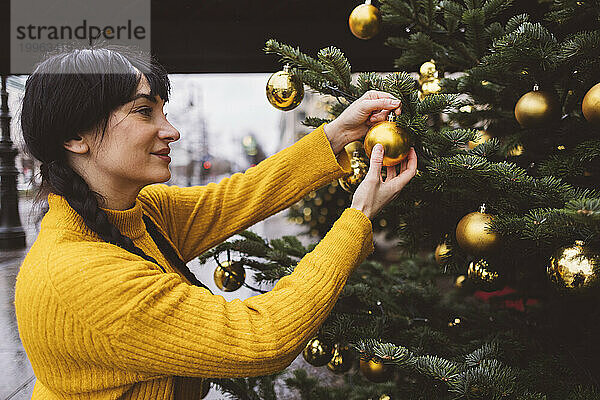 Lächelnde Frau schmückt den Weihnachtsbaum