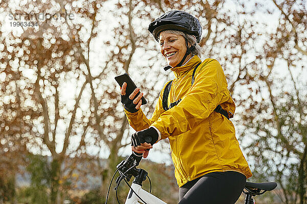 Glückliche Frau  die ihr Mobiltelefon auf dem Mountainbike benutzt