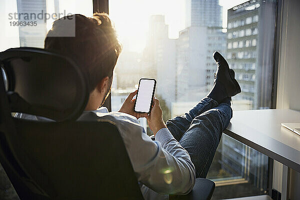 Junger Geschäftsmann entspannt sich und nutzt sein Smartphone im Büro