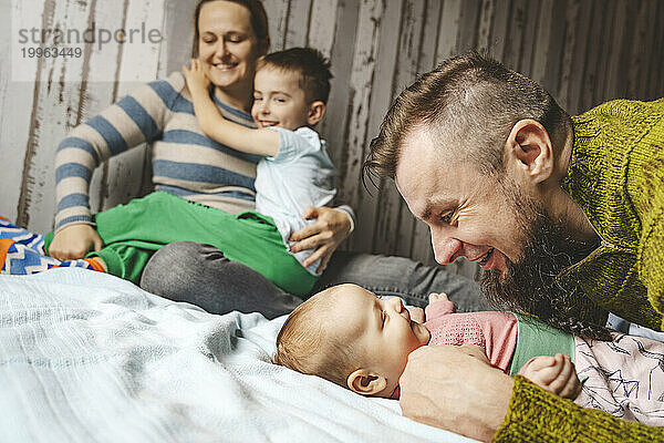 Glücklicher Vater umarmt seine kleine Tochter und Mutter sitzt mit Sohn zu Hause im Bett