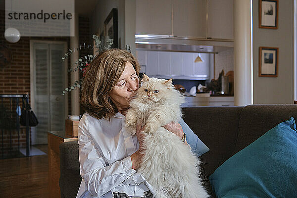 Woman embracing Persian cat and sitting on sofa at home