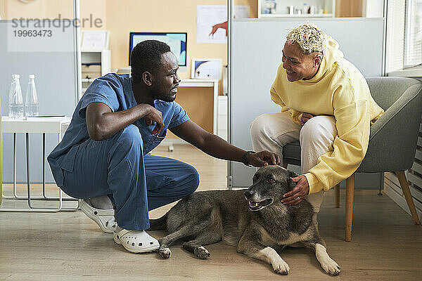 Glückliche Frau spricht mit einem Tierarzt  der den Hund in der Klinik streichelt