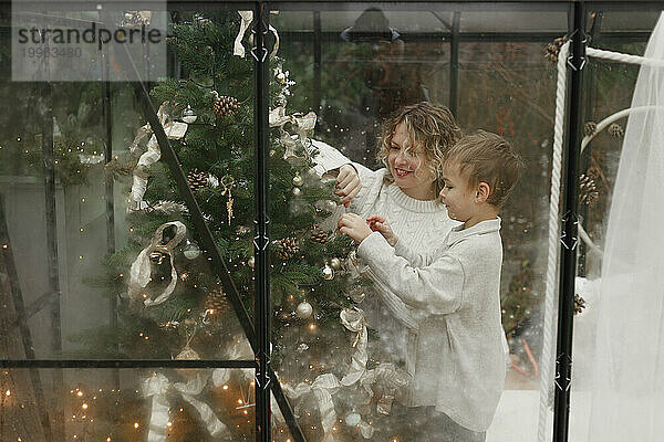 Glückliche Mutter und Sohn schmücken zu Hause den Weihnachtsbaum