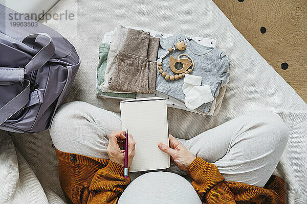 Schwangere Frau bereitet zu Hause Checkliste mit Tagebuch vor