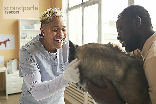 Glücklicher Tierarzt streichelt Hund mit Besitzer in der Klinik