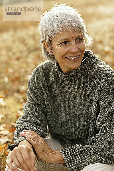 Glückliche Frau mit grauen Haaren sitzt auf dem Feld