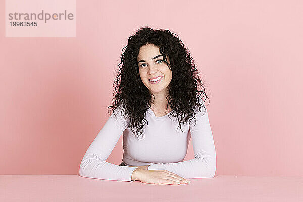 Happy young woman sitting at table against pink background