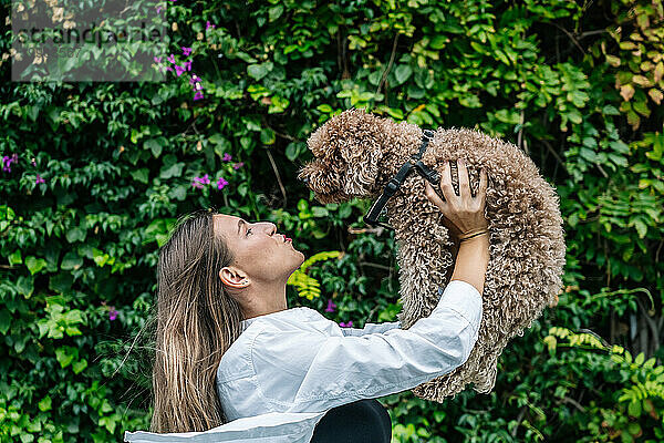 Glückliche junge Frau spielt mit Pudelhund vor Pflanzen