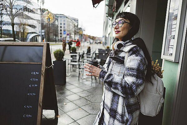 Nachdenkliche Frau mit Kaffeetasse steht im Straßencafé