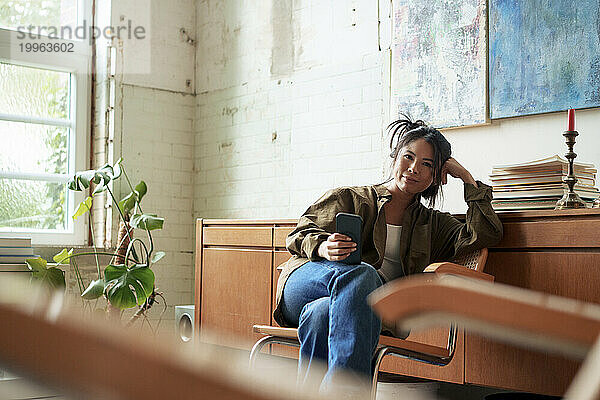 Maler sitzt mit Smartphone in der Werkstatt auf einem Stuhl