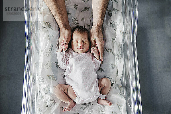 Father holding sleeping baby girl's hands in incubator