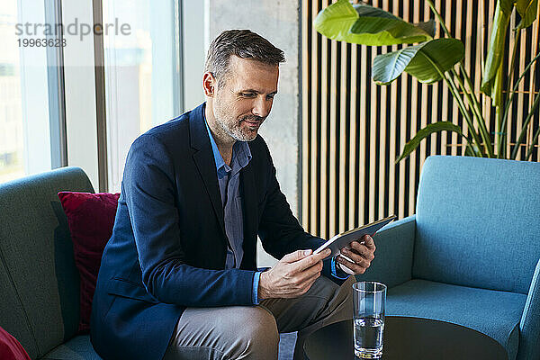 Lächelnder reifer Geschäftsmann nutzt Tablet-PC in der Bürolobby