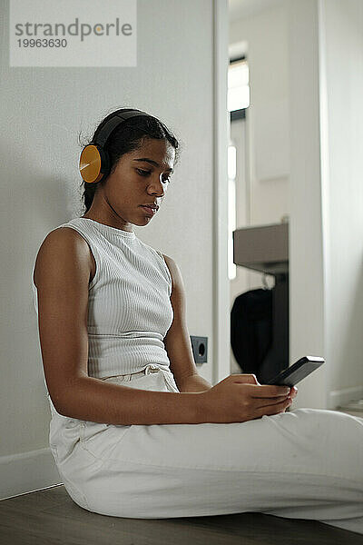 Mädchen trägt Kopfhörer und SMS auf dem Smartphone zu Hause