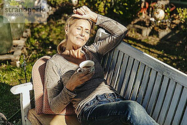 Frau entspannt sich mit einer Tasse Kaffee auf der Gartenbank