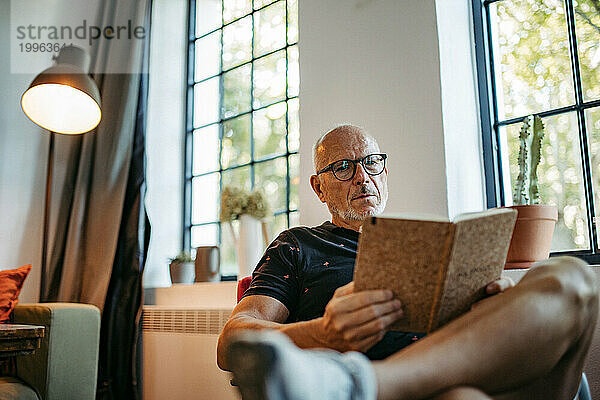 Älterer Mann im Gemeinschaftsraum liest Buch auf Bank sitzend
