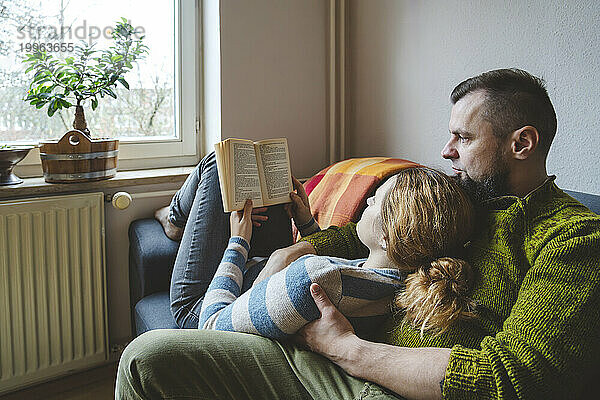 Frau liegt auf dem Schoß eines Mannes und liest zu Hause ein Buch