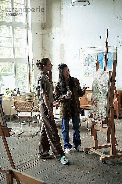 Selbstbewusste Frauen diskutieren über Malerei auf Staffelei im Kunstatelier