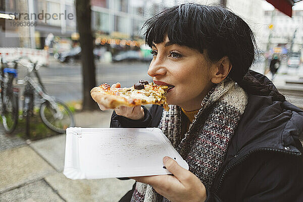 Glückliche Frau  die im Straßencafé ein Stück Pizza isst