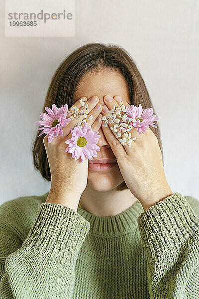 Frau bedeckt Gesicht mit Händen und Blumen vor weißem Hintergrund